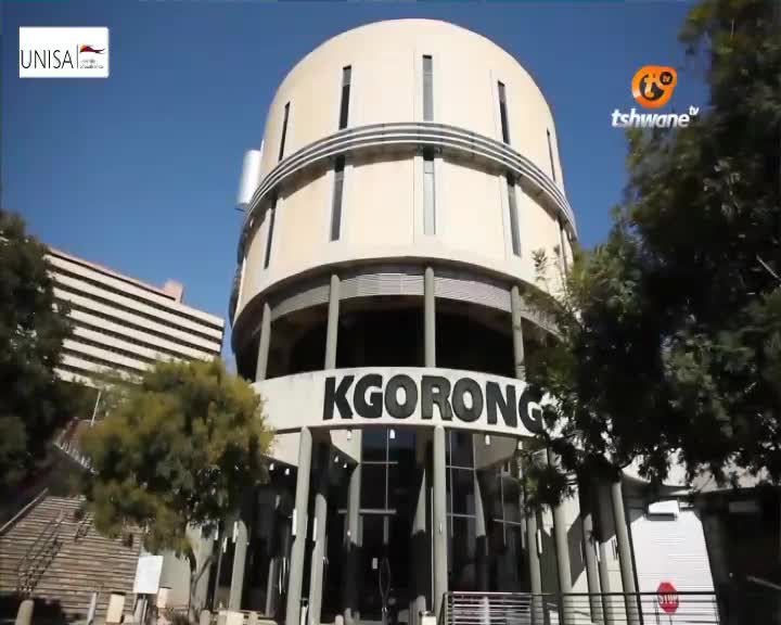 The sun shines on the "KGORONG" building, a distinctive circular structure in Tshwane. Trees frame the entrance, and a UNISA logo is visible on the left. The sun shines on the "KGORONG" building, a distinctive circular structure in Tshwane. Trees frame the entrance, and a UNISA logo is visible on the left.