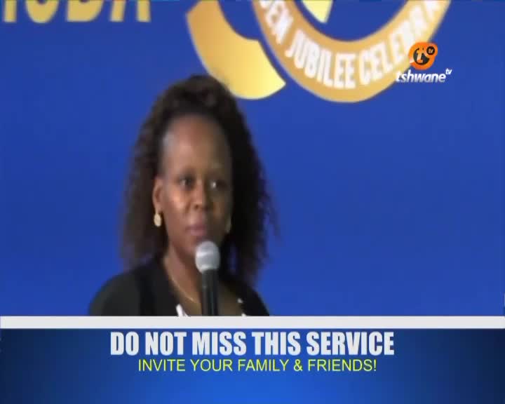 A woman speaks into a microphone, her expression earnest. Behind her, a blue backdrop displays text for a jubilee celebration, with the Tshwane TV logo visible.