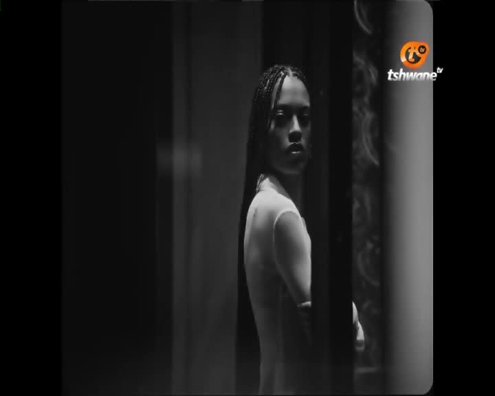 A young woman with braided hair stands in a dimly lit room, her gaze directed outward. The Tshwane TV logo appears in the upper right corner. A young woman with braided hair stands in a dimly lit room, her gaze directed outward. The Tshwane TV logo appears in the upper right corner.