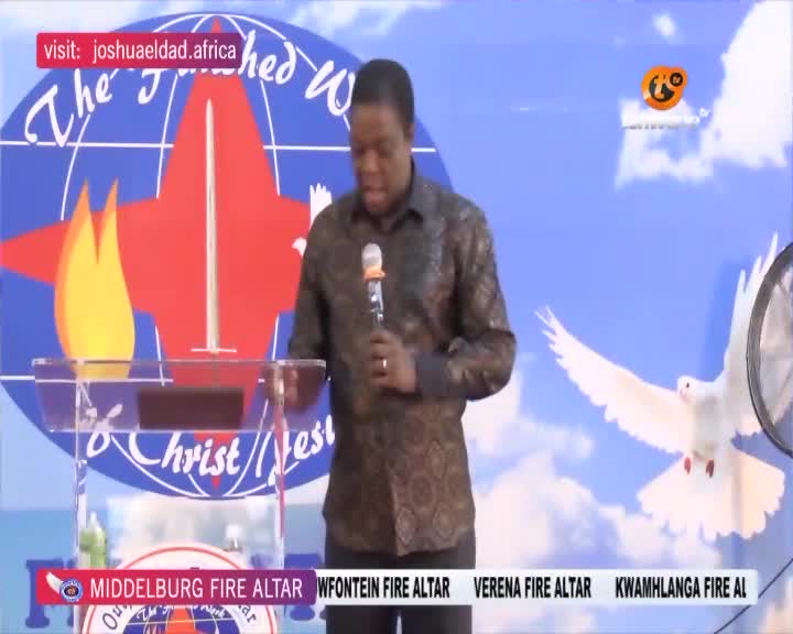 A man in a patterned shirt stands at a clear podium, holding a microphone. Behind him, a large graphic features flames and a dove, with "The Finished Work of Christ" written across it. A banner at the bottom displays "MIDDELBURG FIRE ALTAR" and other locations, suggesting a broadcast from Tshwane. A man in a patterned shirt stands at a clear podium, holding a microphone. Behind him, a large graphic features flames and a dove, with "The Finished Work of Christ" written across it. A banner at the bottom displays "MIDDELBURG FIRE ALTAR" and other locations, suggesting a broadcast from Tshwane.