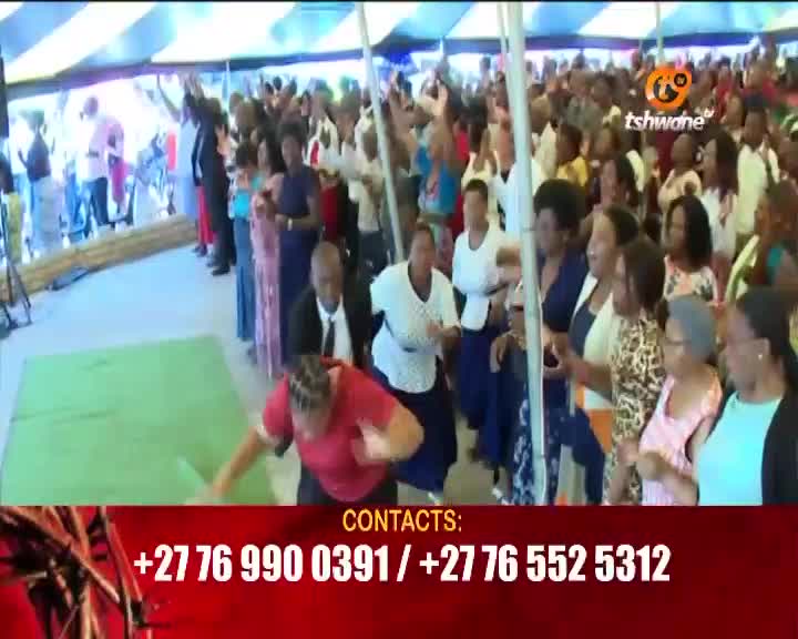A woman in a red shirt is kneeling on a green mat, her hands outstretched. Behind her, a large crowd stands with their arms raised, a common sight at many gatherings in Tshwane. A woman in a red shirt is kneeling on a green mat, her hands outstretched. Behind her, a large crowd stands with their arms raised, a common sight at many gatherings in Tshwane.