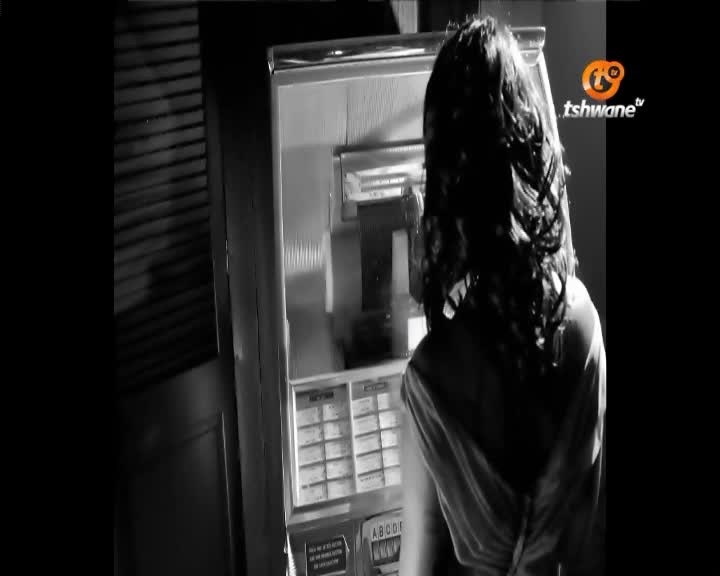 A woman with long, dark hair stands before a jukebox, her back to me. The Tshwane TV logo is visible on the right side of the screen.