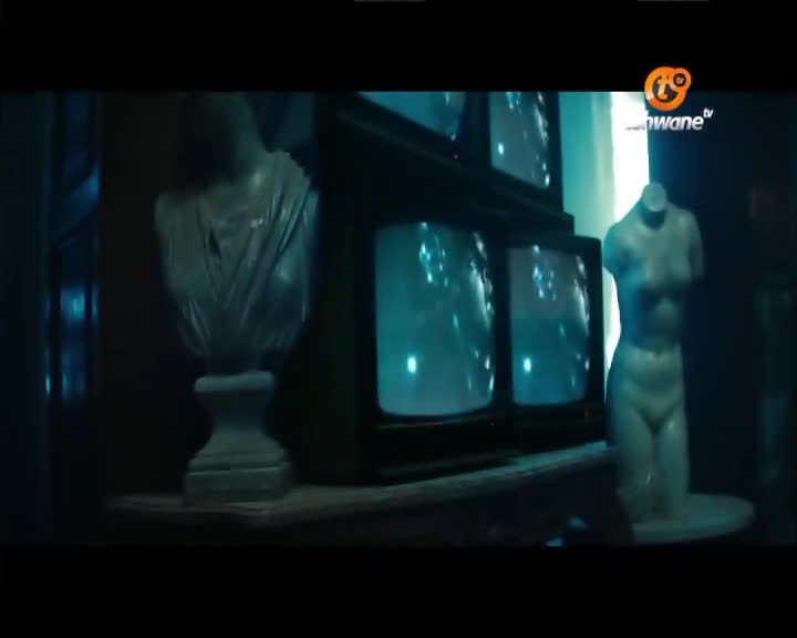 A stack of old televisions hums with static, their screens reflecting a ghostly blue light. Beside them, a headless mannequin stands starkly against the dim interior, a familiar Tshwane TV logo glowing faintly in the corner.