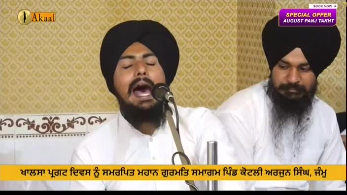 A man with a black turban and beard is speaking into a microphone, his mouth wide open. Beside him, another man in a turban listens, both in a setting that appears to be a broadcast from the Akaal Channel.
