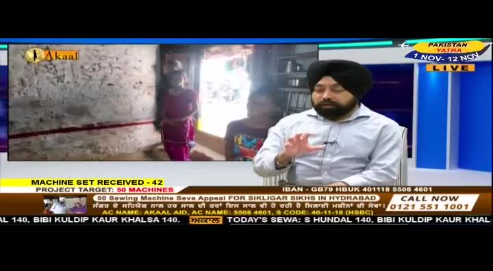 On Akaal Channel, a man in a turban gestures while seated in a studio; behind him, a video shows two children in a simple room. The screen displays text about a sewing machine appeal for Sikhs, with a phone number to call.
