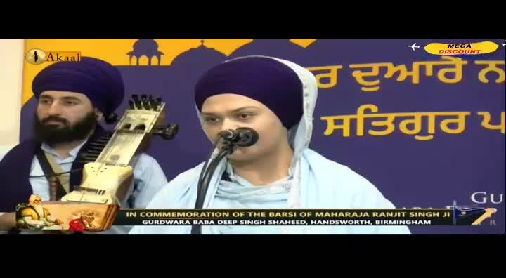 A young man in a turban speaks into a microphone, with a musician beside him holding a stringed instrument. The Akaal Channel logo is visible, and the event is in commemoration of Maharaja Ranjit Singh Ji in Birmingham, United Kingdom.
