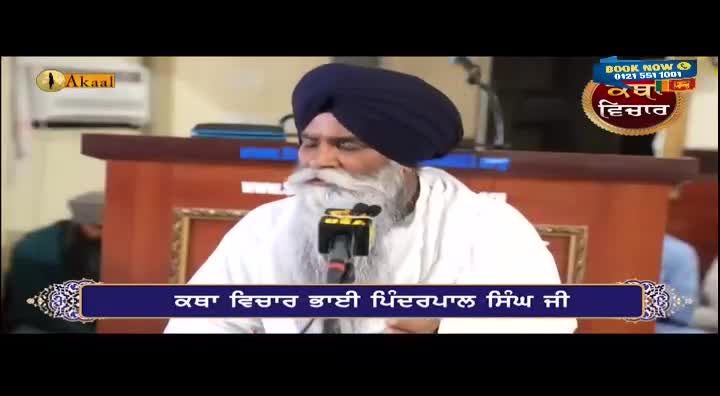 A man with a long white beard and a dark turban is speaking into a microphone. The scene is likely from a broadcast on Akaal Channel in the United Kingdom, with text in Punjabi across the bottom of the screen.
