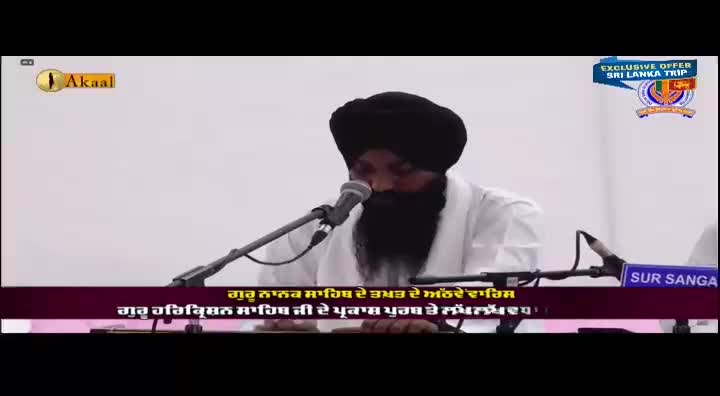 A man in a turban is speaking into a microphone, his words likely broadcast on the Akaal Channel. The screen displays text in Punjabi, and an offer for a trip to Sri Lanka.
