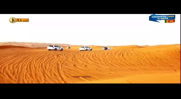 Three white SUVs are kicking up sand as they drive across the dunes, leaving long, parallel tracks behind them. The Akaal Channel logo is in the top left corner.
