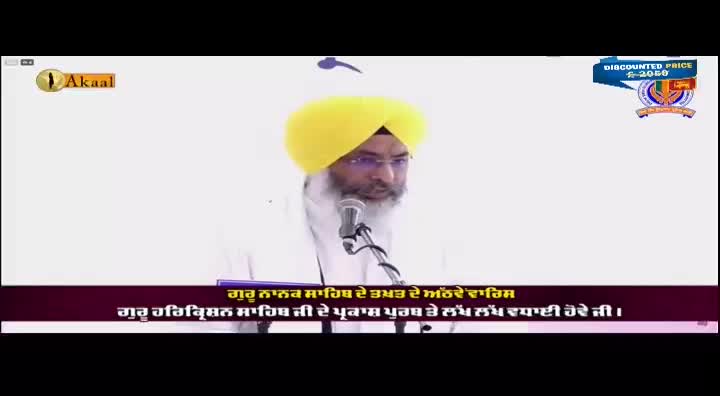 A man with a yellow turban and a long white beard speaks into a microphone, likely on the Akaal Channel. Text in Punjabi appears below him, and a logo is visible in the upper right corner.
