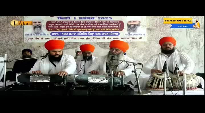 Four men in white robes and orange turbans sit behind instruments, microphones in front of them. The Akaal Channel logo is visible, and a banner with text in Punjabi hangs behind the musicians.
