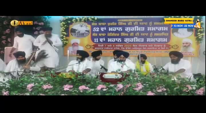 Musicians in white robes and turbans are seated behind instruments and microphones, performing in front of a banner. A logo for Akaal Channel is visible in the top left corner, and a sign indicates the event is the Shaheedi Marg Yatra.
