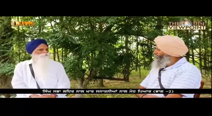 Two men with long white beards and turbans are seated outside, likely in the United Kingdom, conversing on a program for Akaal Channel. The backdrop is a screen with the logo "The Viewpoint" and a caption in Punjabi.
