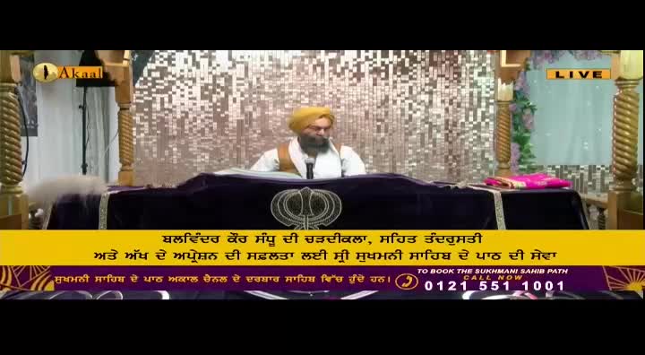 A man with a yellow turban sits behind a dark table, reading. The Akaal Channel logo is visible, and the broadcast is live from the United Kingdom.
