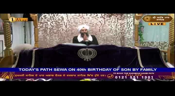A man in a white turban and black suit is speaking from behind a decorated table, with his hands clasped together. The Akaal Channel logo is visible, and a banner states that a Path Sewa is underway.
