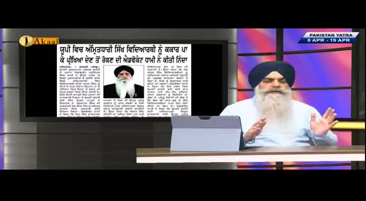 A man with a long white beard and a blue turban speaks animatedly on Akaal Channel, gesturing with his hands. A screen behind him displays a newspaper article with a photo of another man in similar attire.