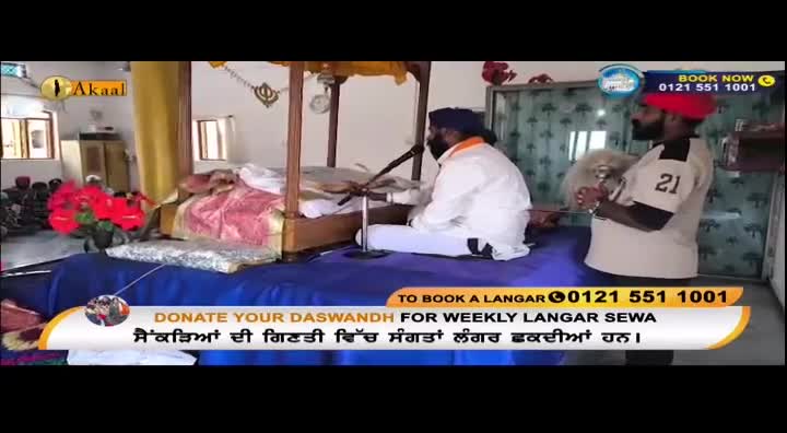 A man in white is seated before a microphone, while another man in a light-coloured shirt with the number 21 on it stands nearby, holding a white object. The Akaal Channel logo is visible in the corner.