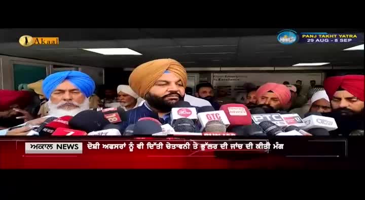 A group of men, some wearing turbans, stand behind a row of microphones, addressing the press. The Akaal Channel logo appears in the corner, and text scrolls across the bottom of the screen.