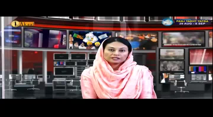 A woman in a pink headscarf speaks directly to the camera, her voice clear and steady. Behind her, multiple screens display news footage, including images of the Panj Takht Yatra.