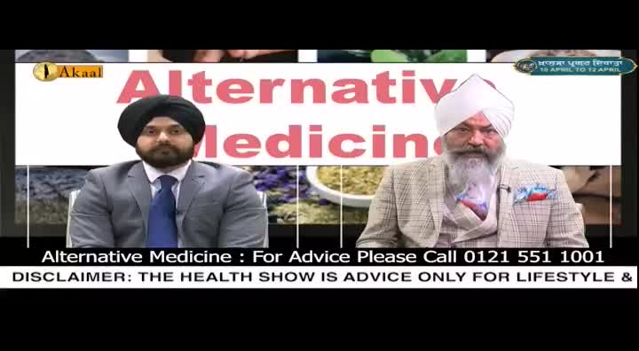 Two men sit on a set with "Alternative Medicine" displayed behind them. The man on the left wears a suit and tie, while the man on the right sports a plaid jacket and a long white beard.