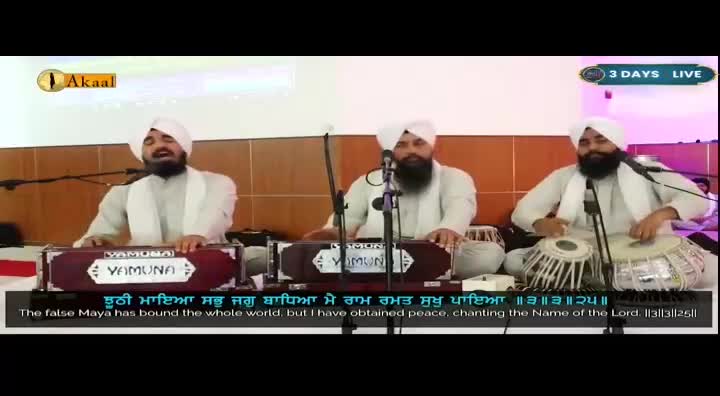 Three men in white turbans are performing devotional music, one singing while playing a harmonium, another on a tabla, and a third also on a harmonium. The Akaal Channel logo is visible, indicating this is a live broadcast from the UK.