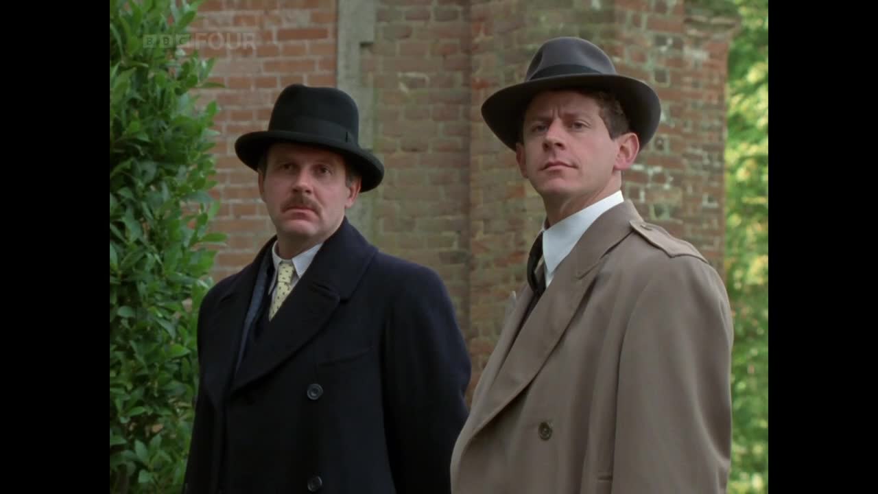 Two men in hats and coats stand side-by-side, their gazes fixed on something just off-camera. The BBC Four logo is visible, suggesting a scene from a United Kingdom production.
