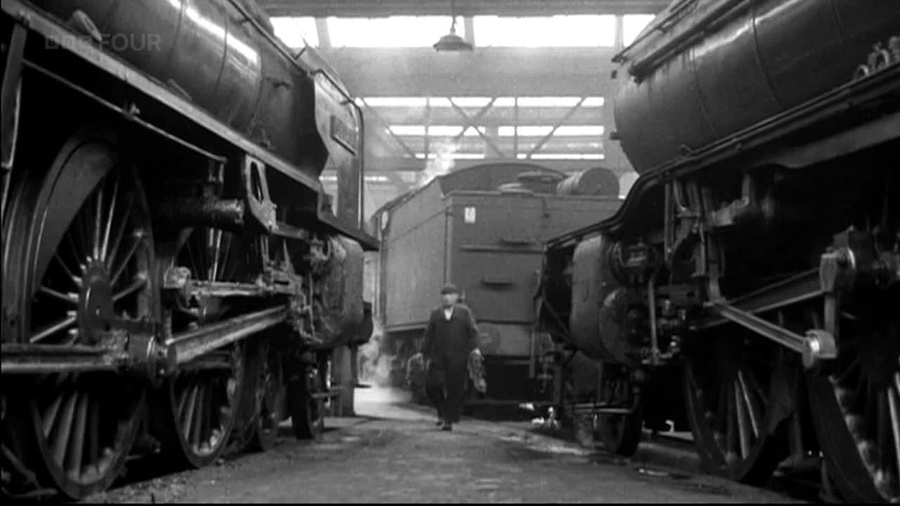A man in a dark coat walks between the hulking, black steam engines. Steam rises from the middle of the scene, and the BBC Four logo is visible in the corner.
