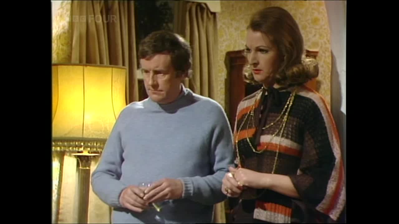 The man, in a light blue sweater, holds a glass and looks concerned. Beside him, a woman in a patterned top stares intently.
The man, in a light blue sweater, holds a glass and looks concerned. Beside him, a woman in a patterned top stares intently.