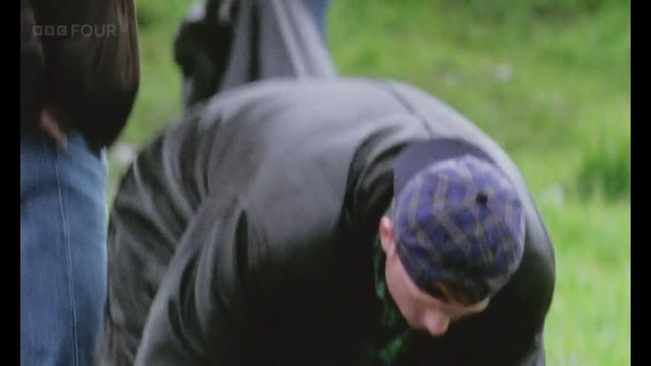 A man in a dark jacket and plaid cap is bent over, his face obscured. He's on a grassy area, likely outdoors, as BBC Four is broadcasting.
A man in a dark jacket and plaid cap is bent over, his face obscured. He's on a grassy area, likely outdoors, as BBC Four is broadcasting.