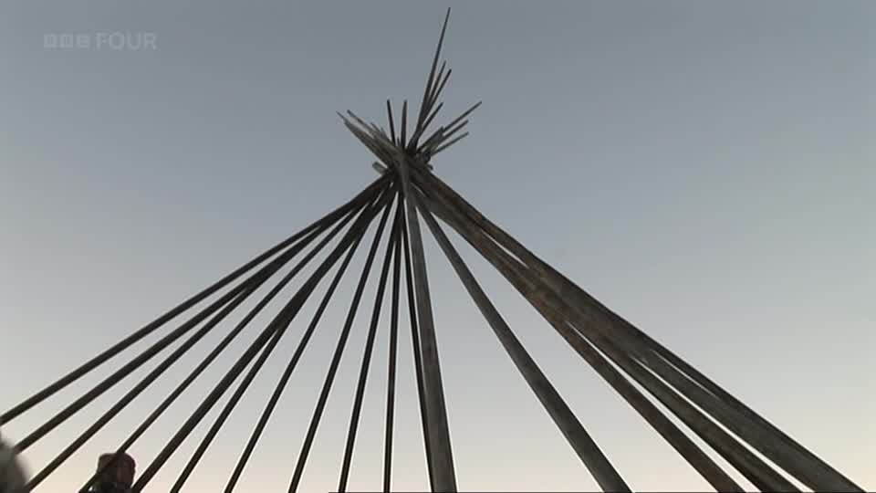 Wooden poles splay outwards, converging at a point against the pale sky, like the ribs of some ancient structure. The BBC Four logo sits unobtrusively in the corner, hinting at a documentary about British heritage.