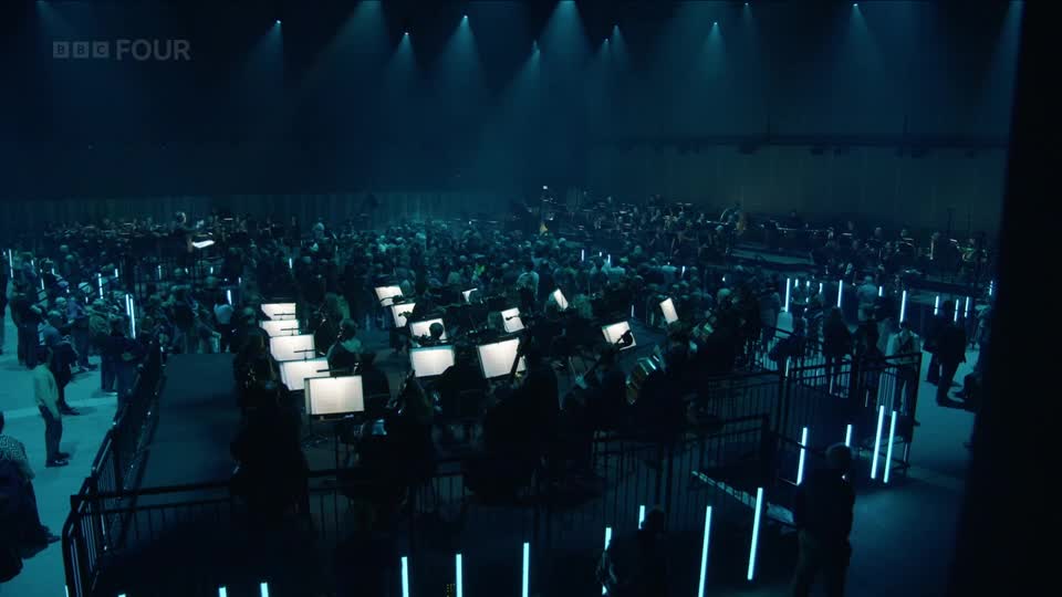 A vast orchestra sits before me, each musician bathed in the glow of their individual screens. The BBC Four logo hangs high above, a silent witness to this unique performance.