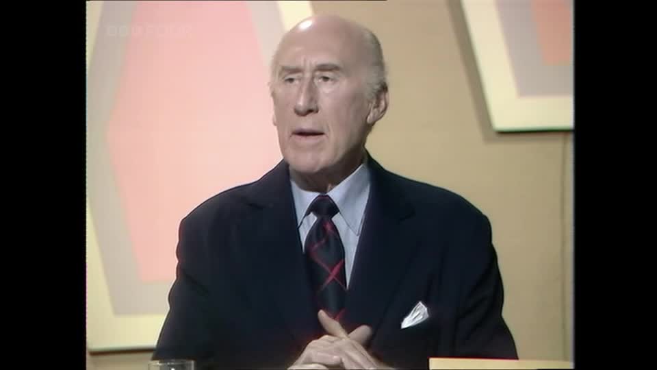 A man in a dark suit and tie speaks into a microphone. The BBC Four logo is visible in the background.