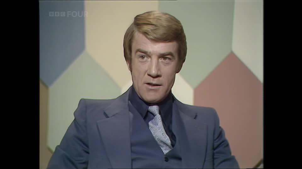 A man in a sharp blue suit and patterned tie speaks directly to the camera. The BBC Four logo appears in the upper left corner of the screen.