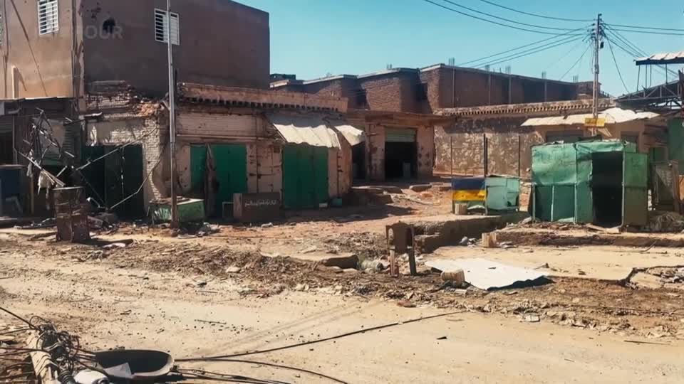 The street is choked with debris, the storefronts on either side showing signs of damage. A lone chair sits precariously on a raised section of rubble.