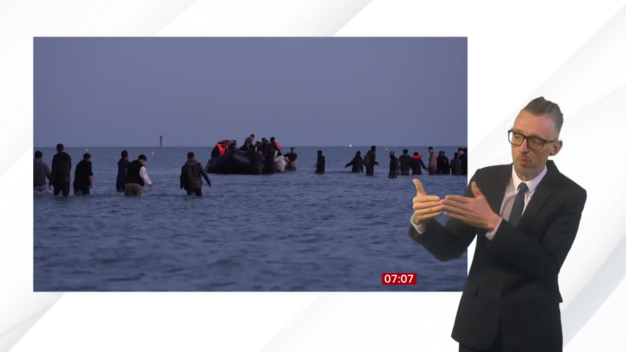 People wade through the water toward the shore, some wearing life vests, while others are still in an inflatable boat. The BBC News coverage shows the scene unfolding under a gray sky.
