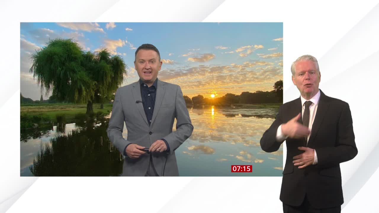 The BBC News weather report shows a tranquil sunrise over a reflective body of water, with a presenter speaking to the camera. Beside him, a man in a suit uses sign language, his gestures mirroring the words.
