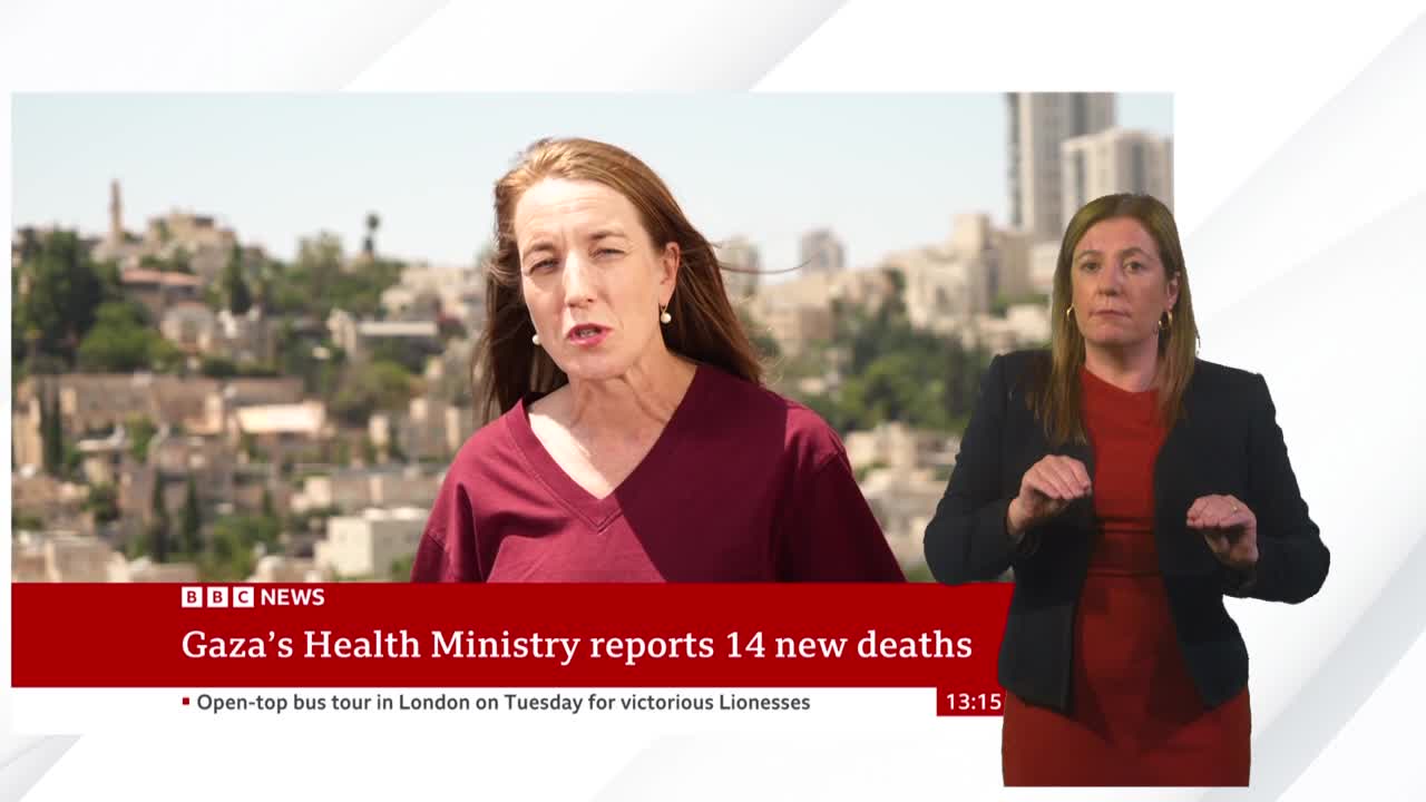 A BBC News report is unfolding, with a presenter speaking against a backdrop of buildings. Beside her, a woman in a red dress and black blazer is signing.
