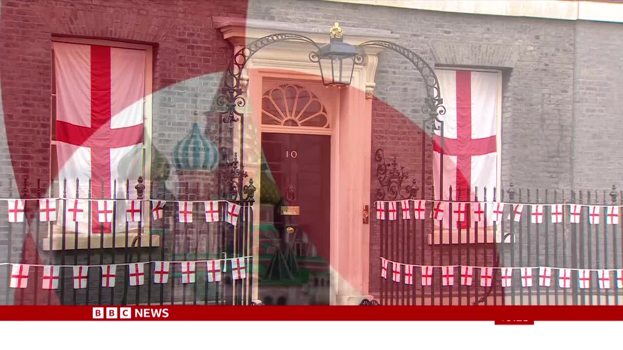 England flags hang from the windows and fence outside number 10, as seen on BBC News. The red and white crosses are prominent against the brick and stone facade.
