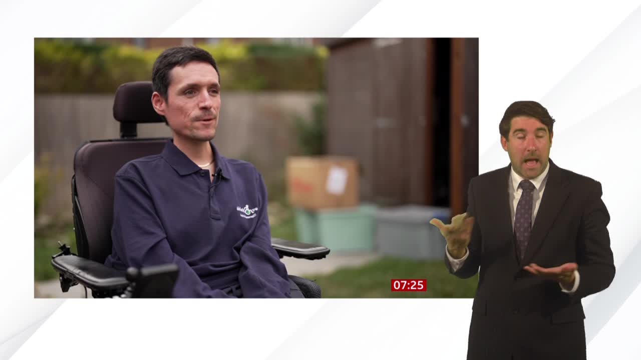 A man in a wheelchair is being interviewed on BBC News, with a presenter gesturing animatedly on the right. The timecode in the corner reads 07:25.
