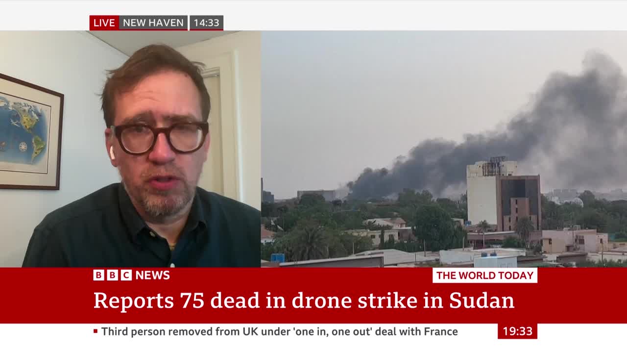 A BBC News presenter in New Haven speaks to the camera, while a scene of thick, dark smoke billowing over buildings in Sudan plays beside him. The lower third of the screen displays the headline "Reports 75 dead in drone strike in Sudan."
