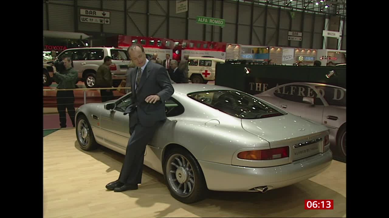 A man in a suit leans casually against a silver sports car, posing for the cameras. Behind him, a BBC News crew films the scene at what looks like a car show in the United Kingdom.
A man in a suit leans casually against a silver sports car, posing for the cameras. Behind him, a BBC News crew films the scene at what looks like a car show in the United Kingdom.