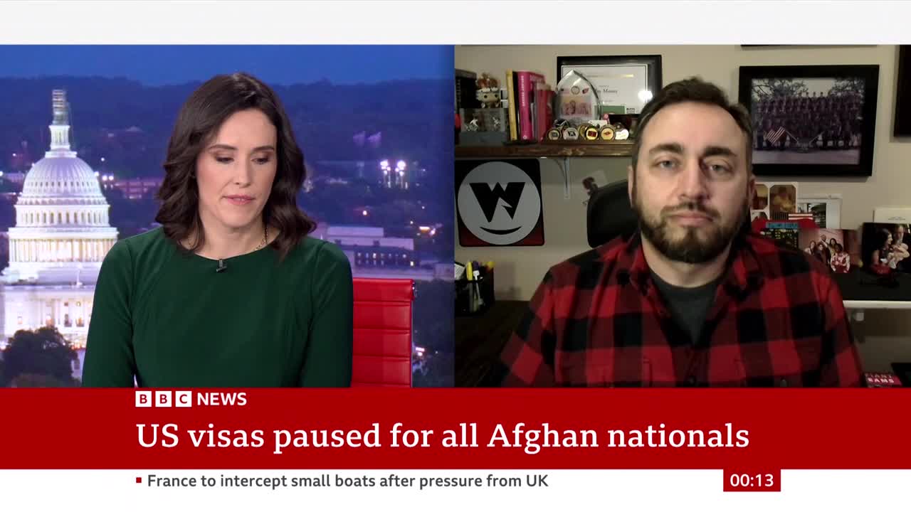 A BBC News broadcast is underway, with a woman in a green dress and a man in a red plaid shirt appearing on screen. The headline states US visas are paused for Afghan nationals.
