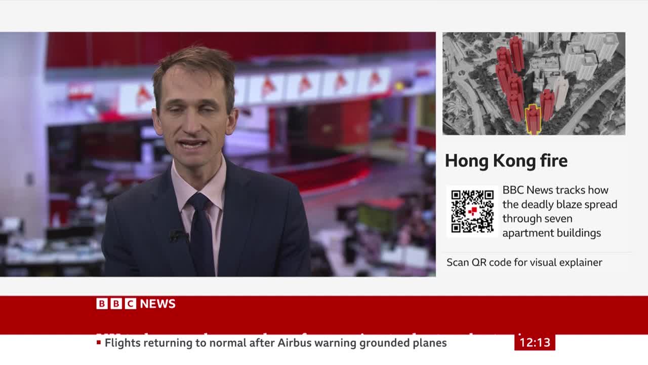 A man in a suit speaks earnestly from a BBC News studio, with a graphic about a fire in Hong Kong displayed beside him. The graphic shows a map of the area with red highlights indicating the affected buildings.
