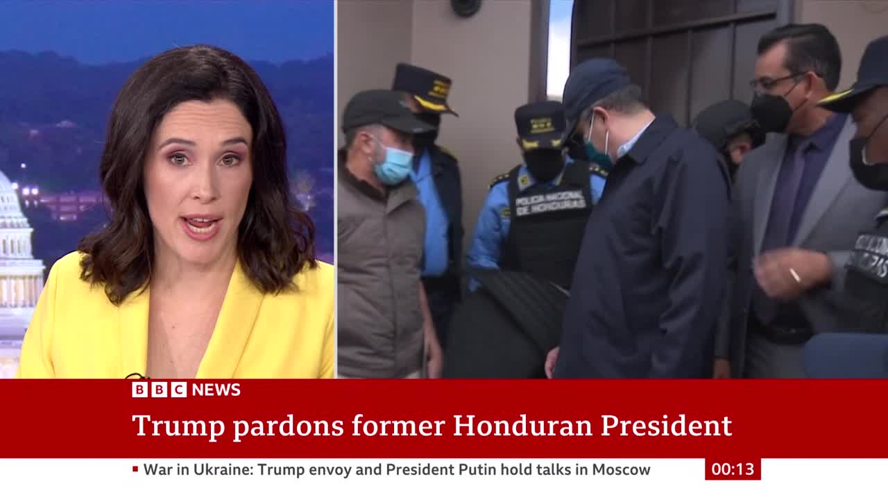 A woman in a yellow blazer speaks directly to the camera, as a news report from the United Kingdom's BBC News unfolds. In the background, a man in a dark jacket is escorted by several individuals, some in uniform.
