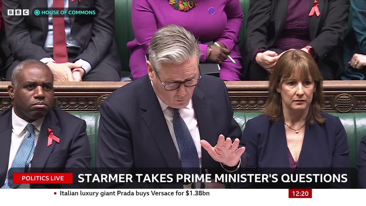 Keir Starmer gestures with his right hand as he speaks, his gaze focused downward.  The BBC News broadcast shows the House of Commons, where a serious atmosphere hangs in the air.
