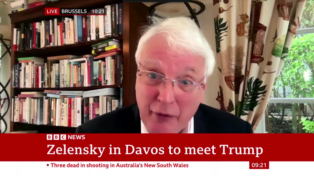 A man with white hair and glasses speaks directly to the camera, a bookshelf behind him. A BBC News chyron at the bottom reads "Zelensky in Davos to meet Trump."