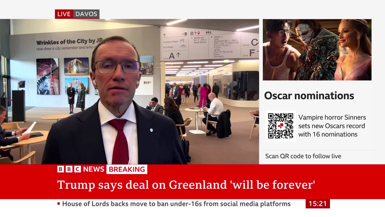A man in a suit speaks directly to the camera, while in the background, people mill about a modern convention center. A BBC News graphic at the bottom announces a statement from Trump regarding Greenland.