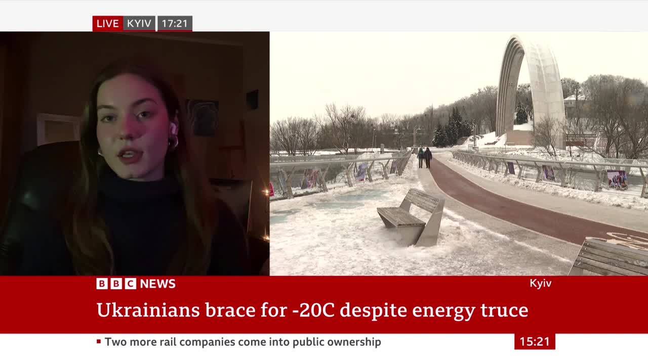 Two figures walk along a snow-covered path beside a frozen river, heading towards a large archway. The BBC News banner below reads "Ukrainians brace for -20C despite energy truce."