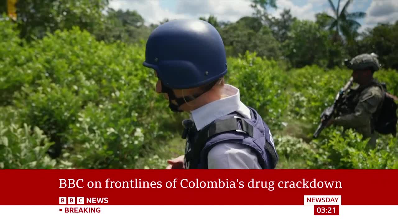 A man in a blue helmet and tactical vest moves through dense green foliage. Behind him, an armed soldier scans the surroundings.