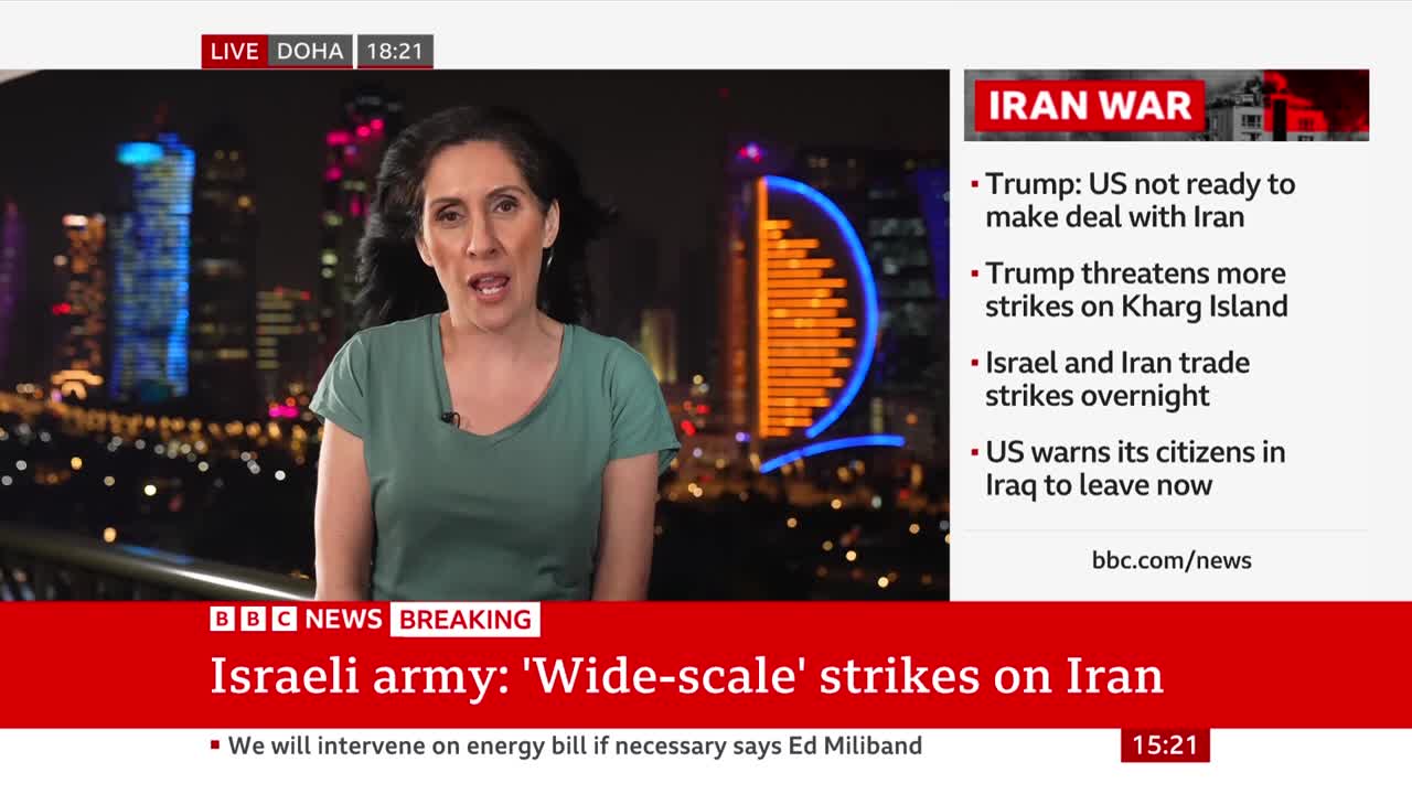 A woman speaks passionately in front of a city skyline at night, with a BBC News banner below detailing "Israeli army: 'Wide-scale' strikes on Iran." The screen also displays breaking news headlines about Iran and the US.